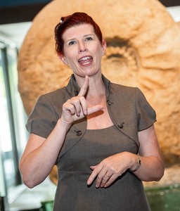 Eine Frau steht vor einem großen Fossil und gibt eine Führung in Gebärdensprache. Eine Frau steht vor einem großen Fossil und gibt eine Führung in Gebärdensprache.